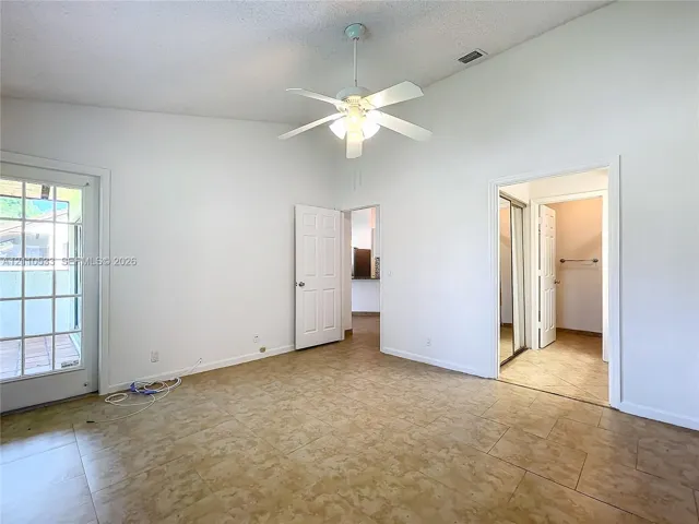 Vaulted ceilings, tile flooring, ceiling fan with integrated lighting, glass-paned exterior door, and built-in closet storage