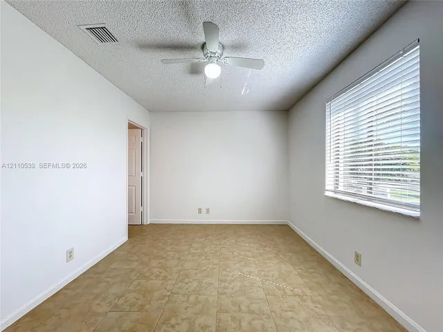 Neutral-toned wall finish, large-format tile flooring, multi-blade ceiling fan with integrated lighting, and horizontal window blinds