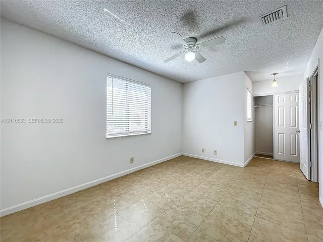 Neutral-toned tile flooring, ceiling fan with integrated lighting, and a closet with a paneled door
