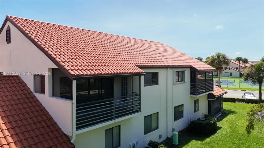 Exterior featuring a clay tile roof, multiple screened-in balconies with horizontal metal railings, and stucco siding