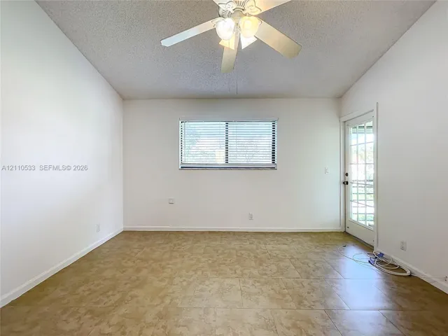 High-ceiling room featuring tile flooring, a multi-blade ceiling fan with integrated light fixture, a horizontal window with blinds, and a glass-paneled exterior door