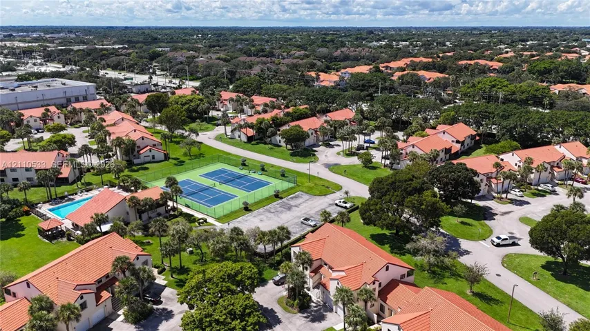Aerial perspective featuring a community tennis court, a swimming pool, and tiled-roof residential structures set within landscaped grounds