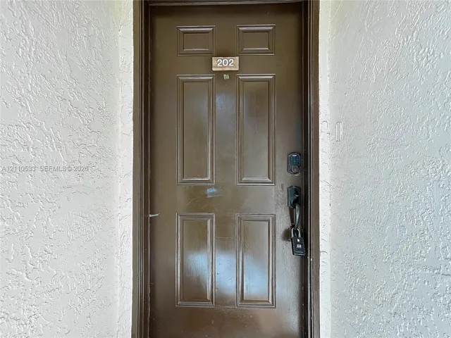 Brown six-panel entry door featuring a matte black handle set, electronic keypad lock, and unit numbering