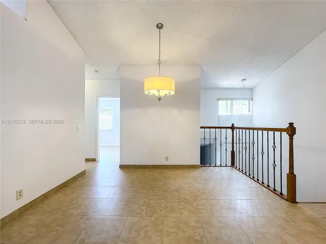 Ceramic tile flooring, drum-style chandelier lighting, and a staircase featuring a wood handrail with metal balusters