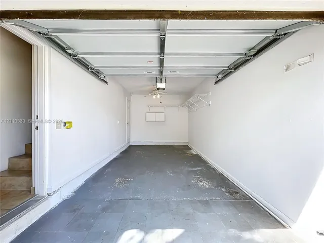 Attached garage featuring a concrete floor, built-in wall shelving, an automatic overhead door opener, and a ceiling-mounted light fixture