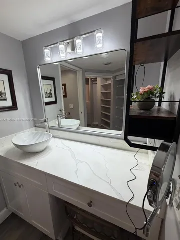 White vanity with a stone-finish countertop, round vessel sink, chrome faucet, rectangular mirror, and a four-light fixture