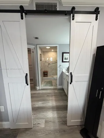 White barn-style sliding doors with black hardware, wood-finish flooring, white cabinetry, and shower enclosure with wall-mounted grab bars