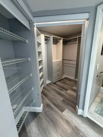 Walk-in closet featuring wood-finish flooring, built-in shelving, integrated dresser drawers, and metal wire rack storage