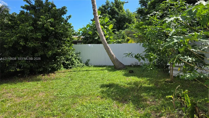 Private backyard featuring a grass lawn, mature trees, and a white privacy fence