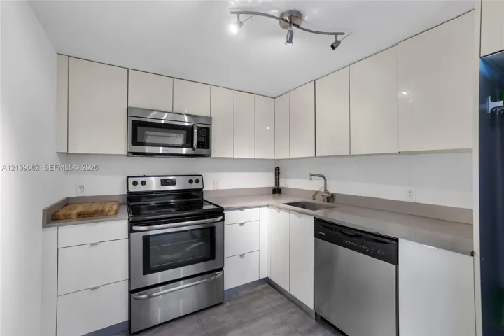 Kitchen featuring flat-panel white cabinetry, solid-surface countertops, integrated stainless steel appliances, stainless steel sink with gooseneck faucet, and adjustable track lighting