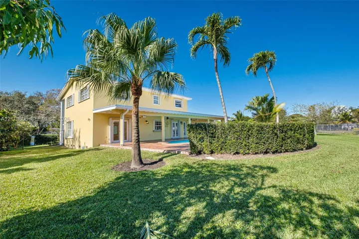 Two-story exterior featuring a covered patio, swimming pool, manicured lawn, and mature palm trees