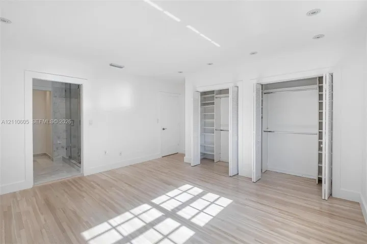 Room featuring wood-finish flooring, recessed lighting, dual closets with built-in shelving, and entry to a stone-tiled shower