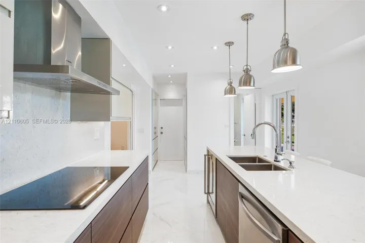 Modern kitchen featuring wood-finish flat-panel cabinetry, light-toned stone-look countertops, stainless steel appliances, marble-patterned flooring, and three pendant lights