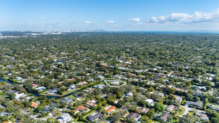 Aerial perspective of a residential lot featuring mature tree canopy, canal frontage, and suburban greenery