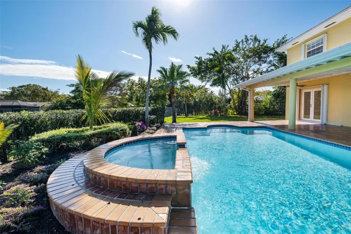 In-ground swimming pool with an integrated elevated spa, brick-tiled coping, covered patio, and mature palm landscaping