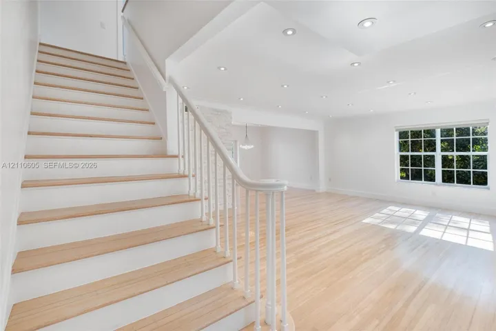 Open interior featuring wood-finish flooring, staircase with white railings, recessed lighting, and multi-pane window