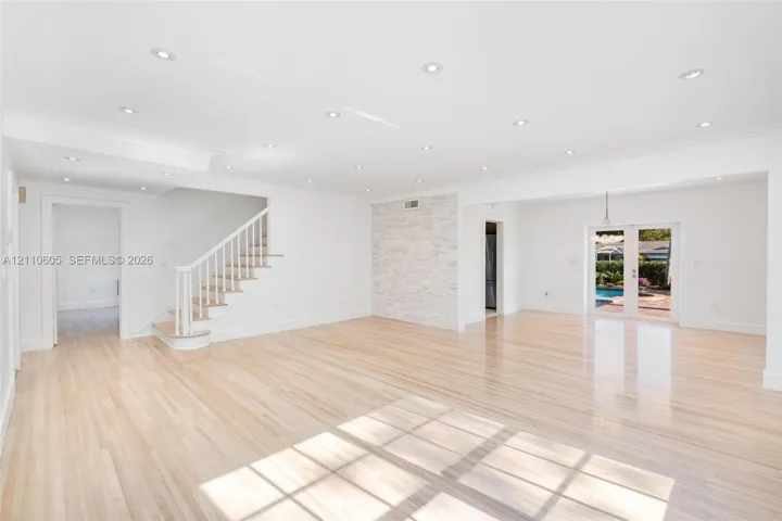 Open-concept interior featuring light wood-finish flooring, recessed lighting, a stone-accented wall, and white staircase railing
