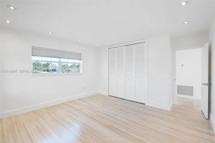 Neutral-toned interior featuring wood-finish flooring, recessed lighting, white louvered closet doors, and a window with a roller shade