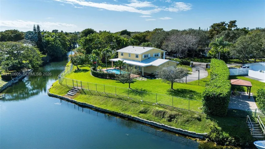 Waterfront property featuring a two-story residence, an in-ground swimming pool, a sprawling grass lawn, a paved driveway, and a detached gazebo