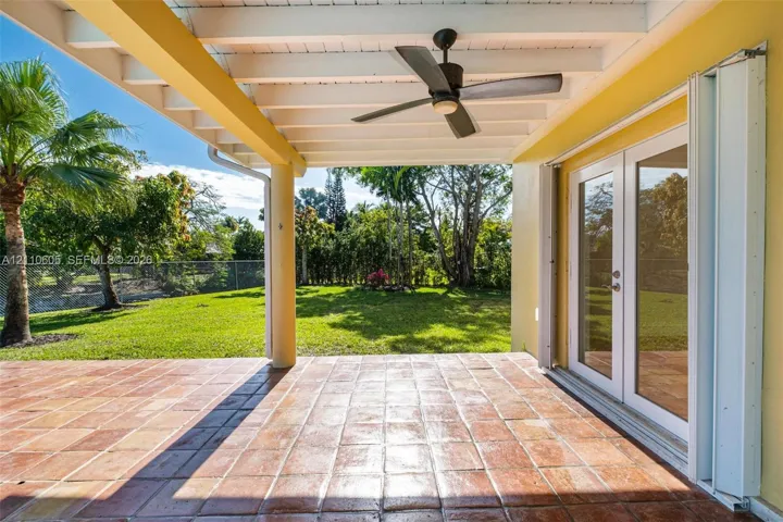 Covered patio featuring terra cotta tile flooring, a sloped wood-beam ceiling with a central fan, and double-glass paneled doors