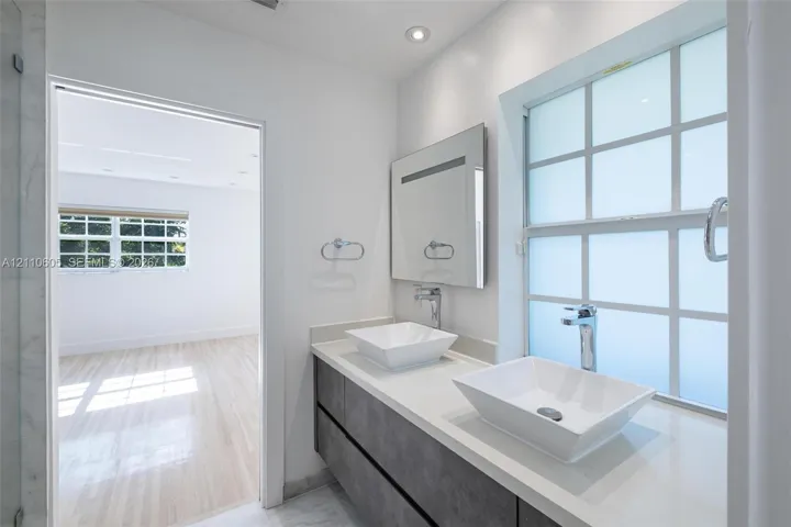 Floating vanity featuring dual rectangular vessel sinks, a solid-surface countertop, modern chrome hardware, and a grid-patterned privacy window