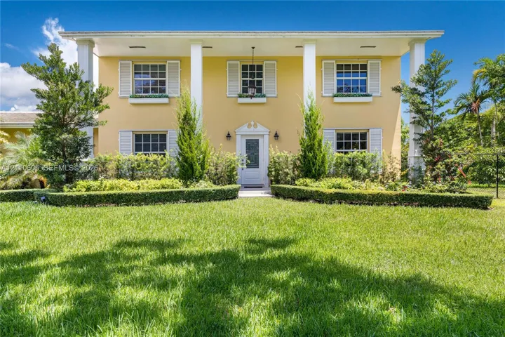 Two-story colonial exterior featuring a covered front porch, prominent structural columns, multi-pane windows with louvered shutters, and window box planters