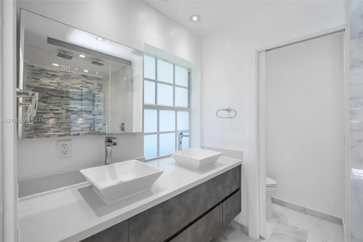 Floating dual-sink vanity with matte-finish cabinetry, white solid-surface countertops, rectangular vessel sinks, and a large frameless mirror
