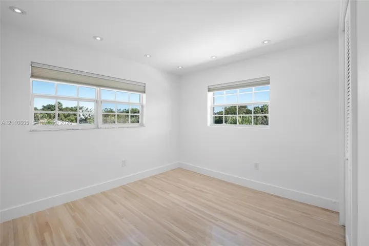 Interior space featuring wood-finish flooring, recessed lighting, multi-pane windows with fitted shades, and louvered closet doors