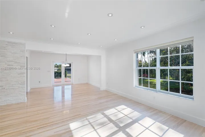 Light-filled interior featuring wood-finish flooring, recessed lighting, a stone-textured accent wall, multi-pane windows, and glass-paned double doors