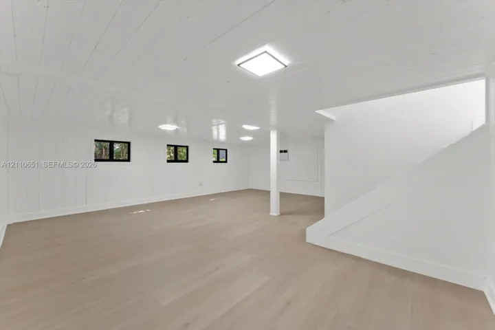 Finished interior space featuring wood-finish flooring, white paneled walls, a painted wood-plank ceiling, square LED flush-mount lighting, and multi-pane windows with black frames
