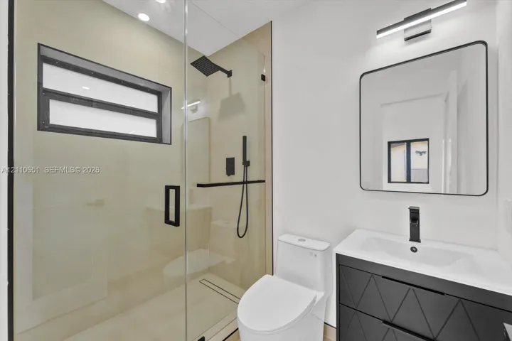 Bathroom featuring a glass-enclosed walk-in shower with matte black rainfall showerhead and handheld sprayer, geometric-patterned vanity cabinet, integrated sink, and modern rectangular mirror with integrated lighting