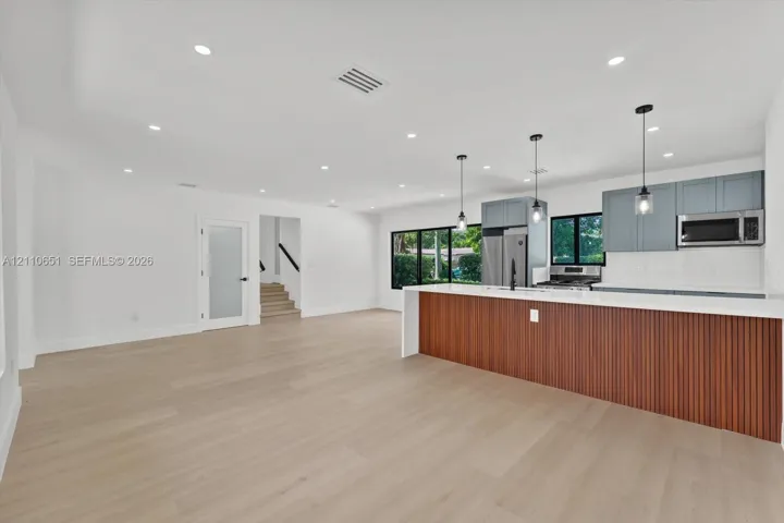 Open-concept kitchen featuring a wood-slat peninsula, quartz countertops, recessed lighting, glass-pane door, and light wood-finish flooring