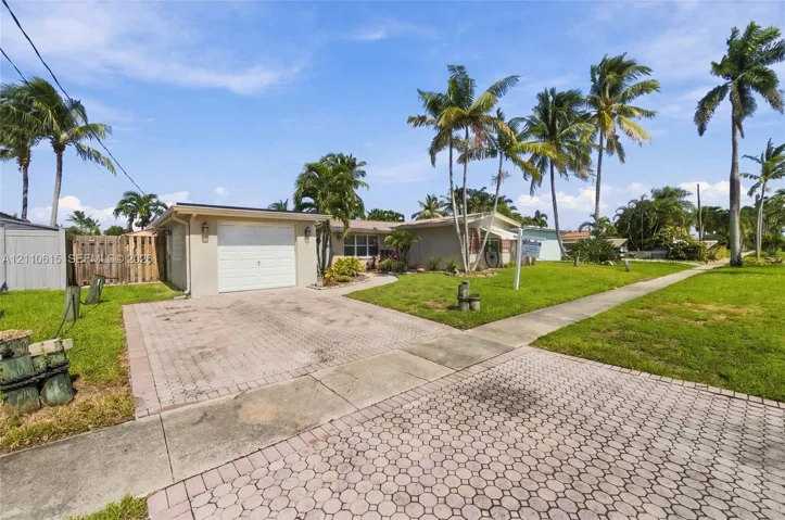 Single-story exterior featuring a paved driveway, one-car garage, manicured lawn, and mature palm trees