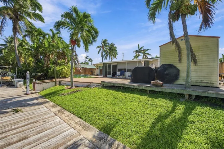 Outdoor space featuring a wooden deck, a grass lawn, a paved patio, and mature palm trees