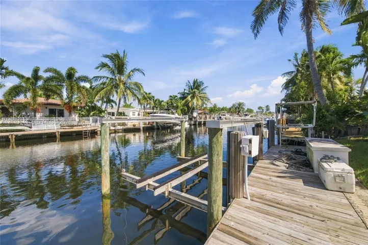 Waterfront property featuring a wood-plank dock, integrated boat lift, and piling-mounted utility housing
