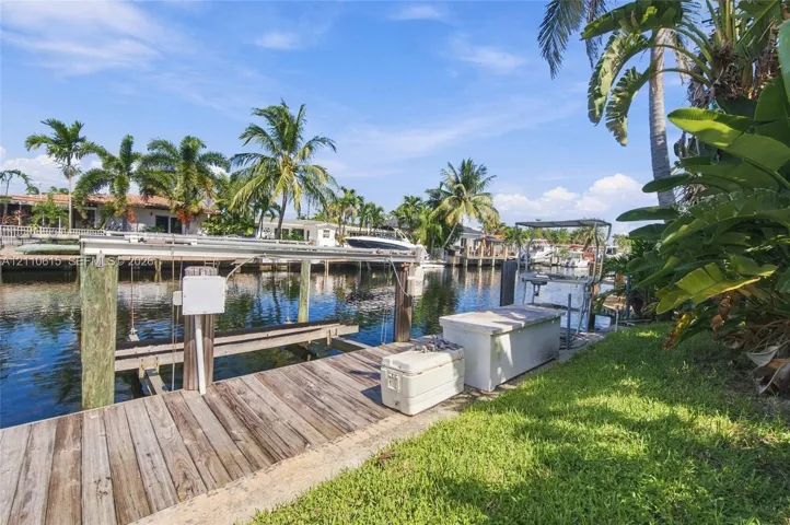 Waterfront property featuring a wooden boat dock, pilings, integrated boat lift, and mature palms