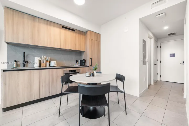 Kitchen featuring wood-finish flat-panel cabinetry, full-height tile backsplash, integrated stainless steel appliances, and large-format tile flooring