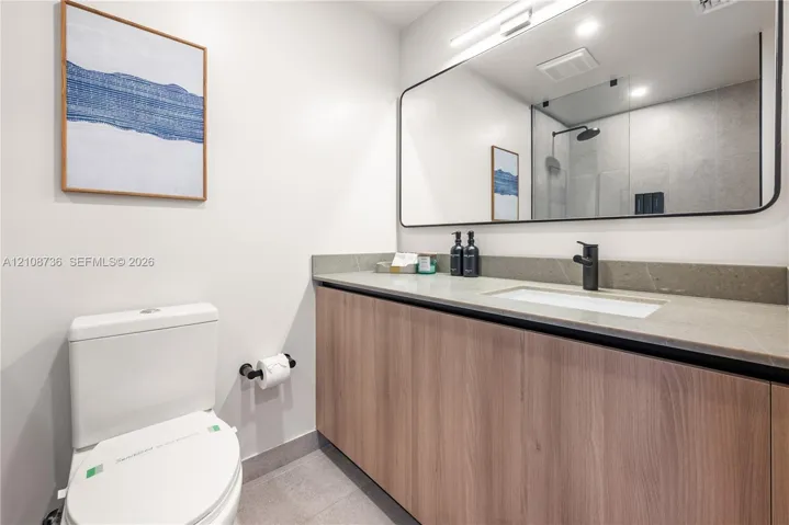 Modern vanity featuring light wood-finish cabinetry, a solid surface countertop, an undermount sink, and matte black fixtures, complemented by a large, frameless rectangular mirror