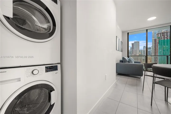 Stacked white front-load laundry unit, floor-to-ceiling windows, and tile flooring