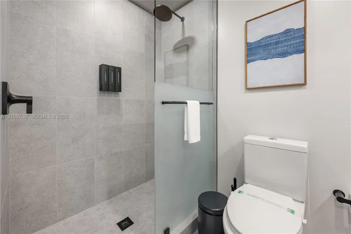 Walk-in shower featuring large-format grey tile, a glass partition with a frosted privacy panel, and matte black fixtures including a wall-mounted shower head and faucet