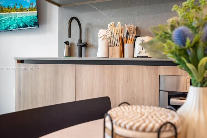 Kitchen area featuring flat-panel wood-finish cabinetry, a matte black high-arc faucet, and a stone-finish backsplash with integrated countertop
