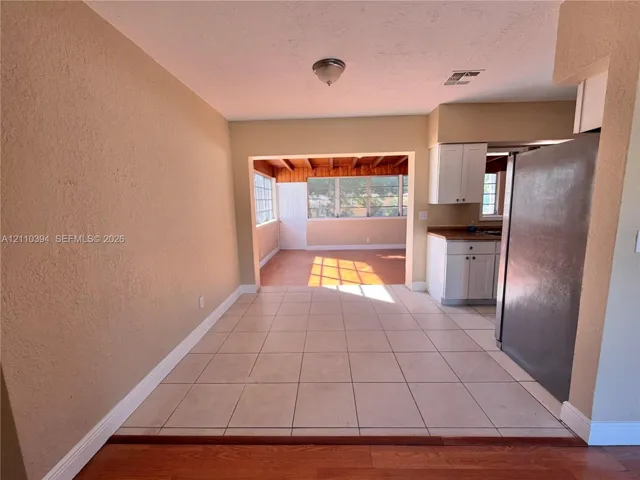 Ceramic tile flooring, white kitchen cabinetry, stainless steel refrigerator, and exposed wooden ceiling beams