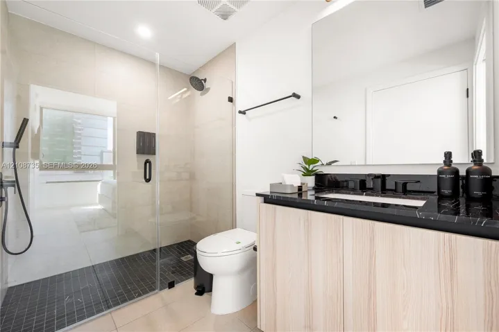 Bathroom featuring a floating vanity with a dark-toned stone countertop, walk-in shower with a glass enclosure and handheld shower head, and large-format wall tiling
