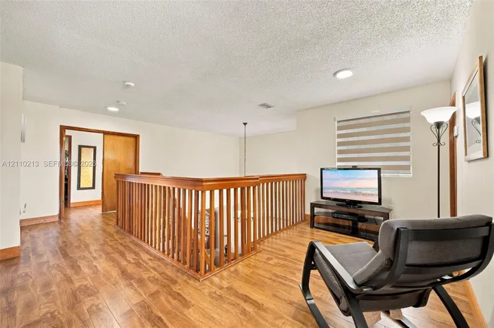 Wood-finish flooring, custom wooden staircase railing, recessed lighting, and dual-layered window shades