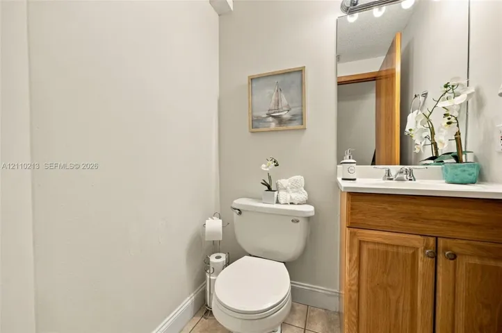 Wood-finish cabinetry, solid-surface countertop with integrated basin, polished chrome faucet, full-width vanity mirror, and ceramic tile flooring