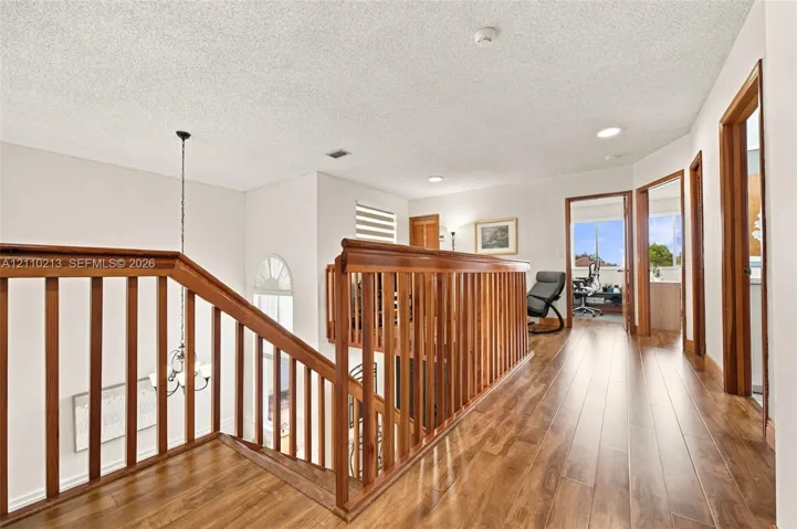 Landing area featuring wood-finish flooring, wood balustrade railing, recessed lighting, and a multi-tiered hanging light fixture