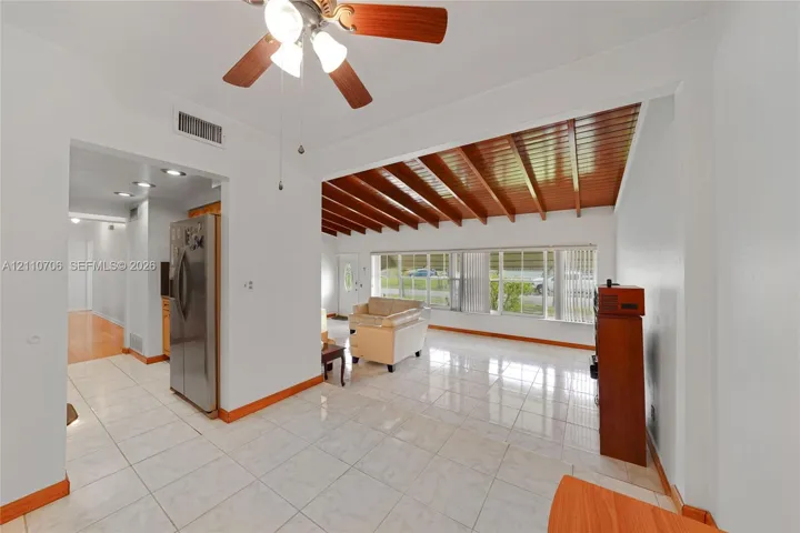 Vaulted wood-plank ceiling, expansive ceramic tile flooring, large multi-pane windows, and a stainless steel built-in refrigerator