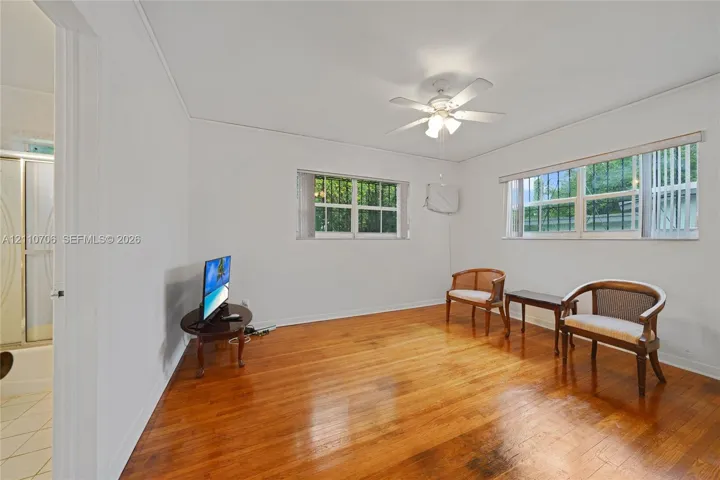Interior space featuring wood-finish flooring, white walls, multiple windows, and a ceiling fan with integrated lighting