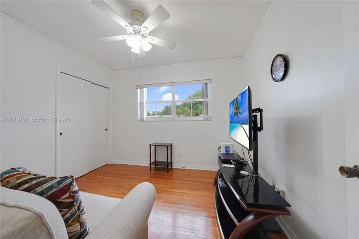 Room featuring wood-finish flooring, a multi-blade ceiling fan with integrated lighting, and a sliding-door closet