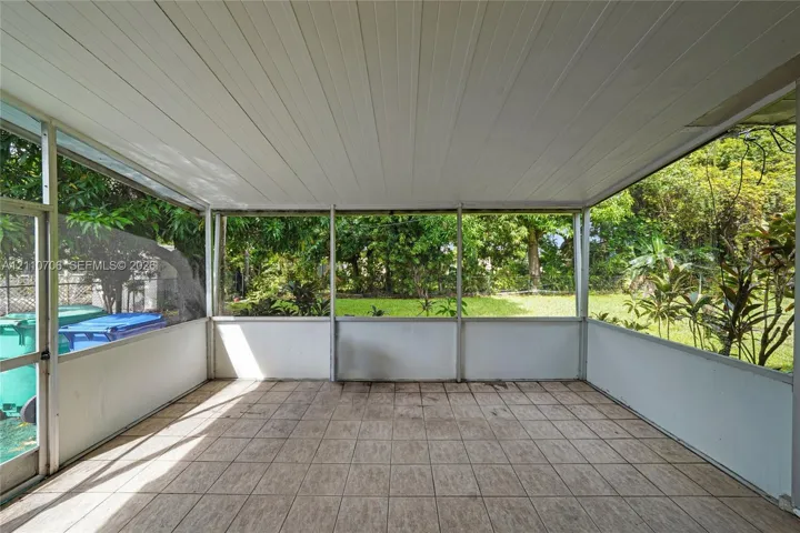 Screened-in porch featuring a solid roof, neutral tile flooring, aluminum framing, and access to a fenced backyard